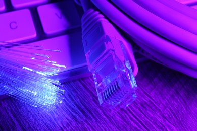 Photo of Optical fiber strands transmitting color light near cable with modular connector and computer keyboard on table, closeup