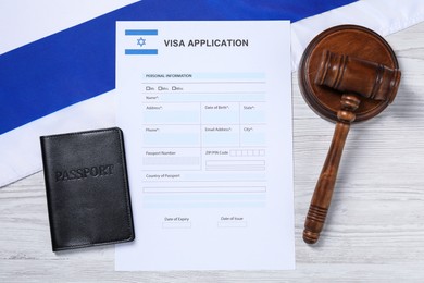 Photo of Immigration to Israel. Visa application form, gavel, passport and flag on white wooden table, flat lay