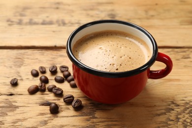 Photo of Cup of aromatic coffee and beans on wooden table, closeup