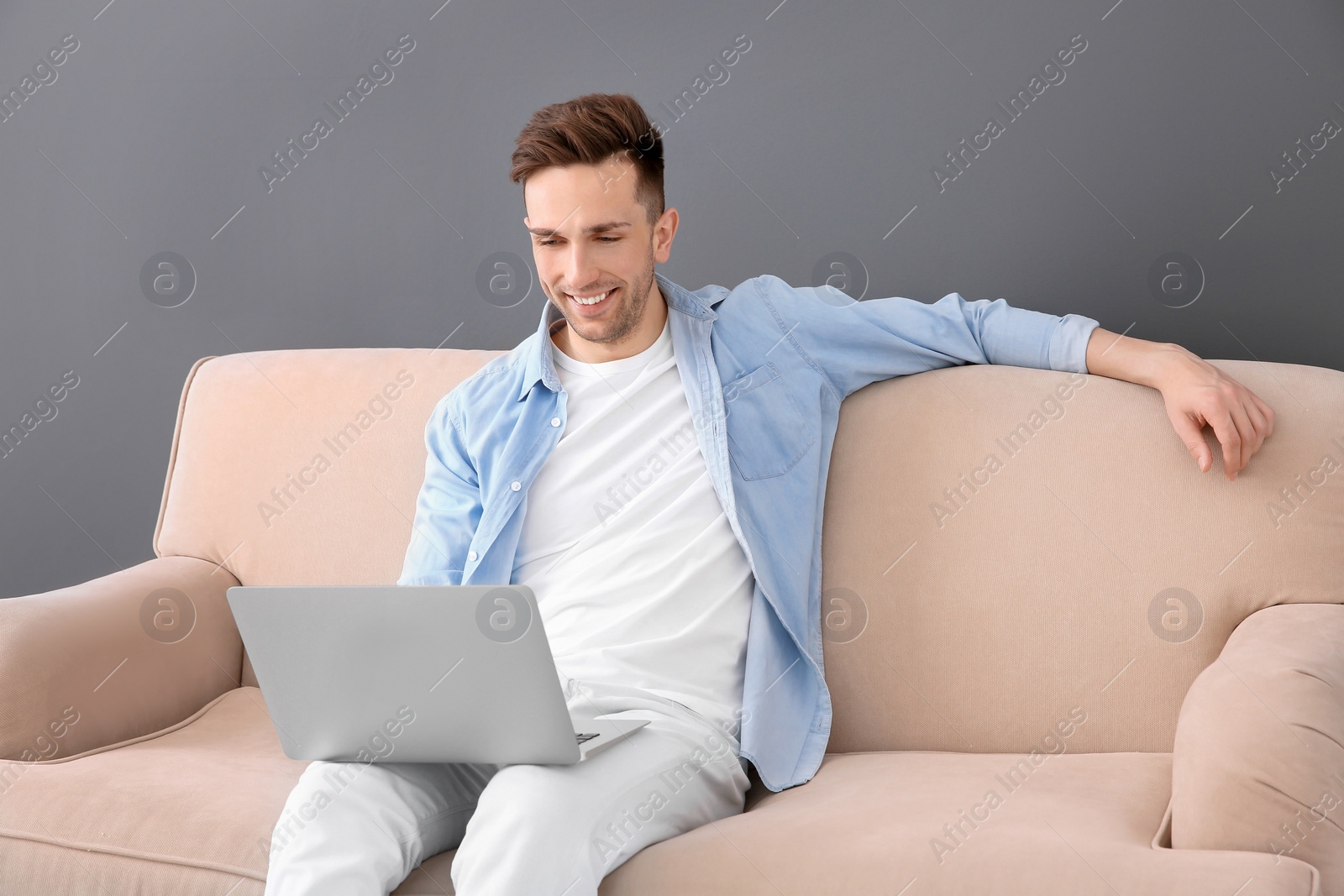 Photo of Handsome young man with laptop sitting on sofa, indoors