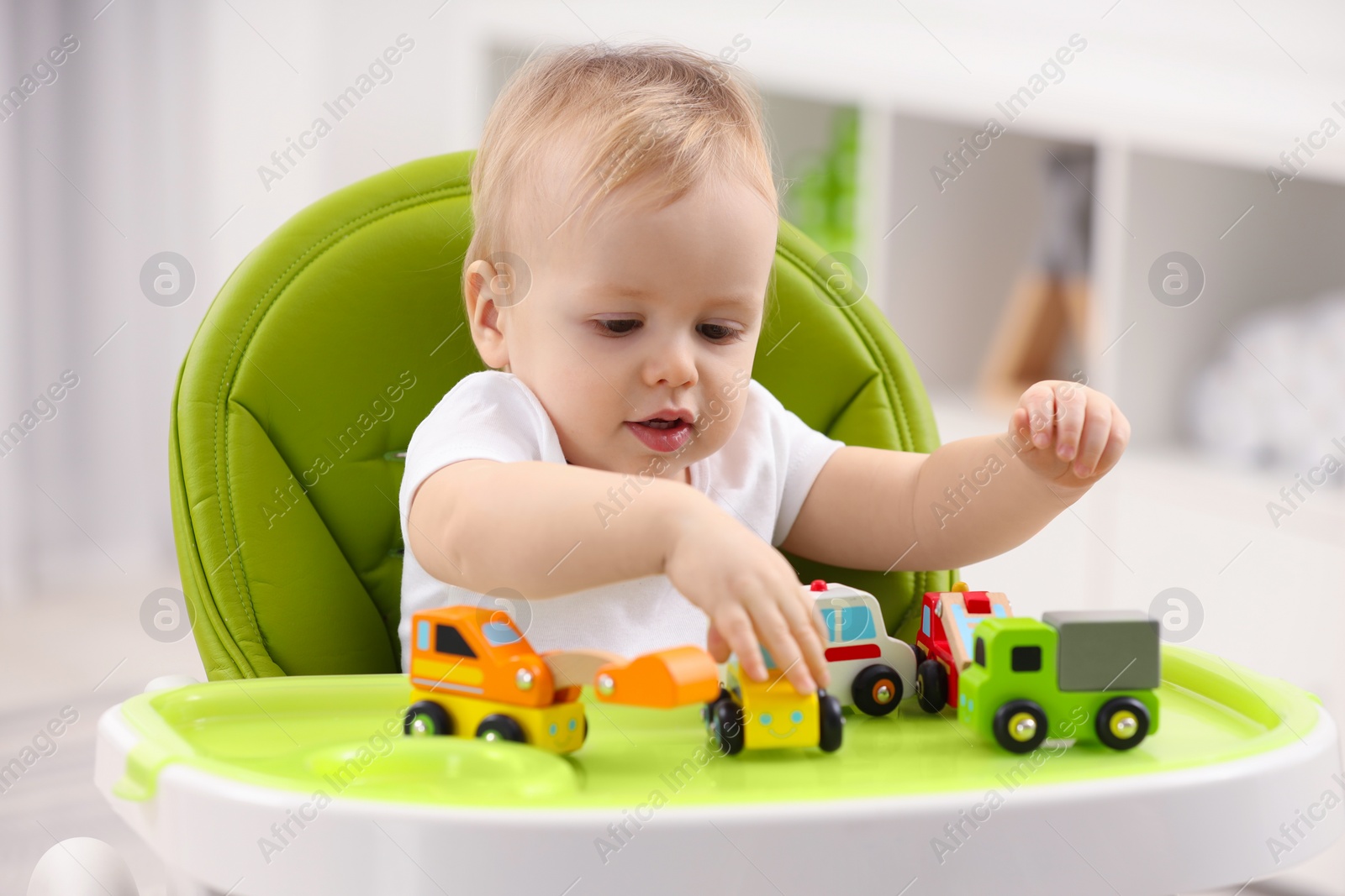 Photo of Children toys. Cute little boy playing with toy cars in high chair at home