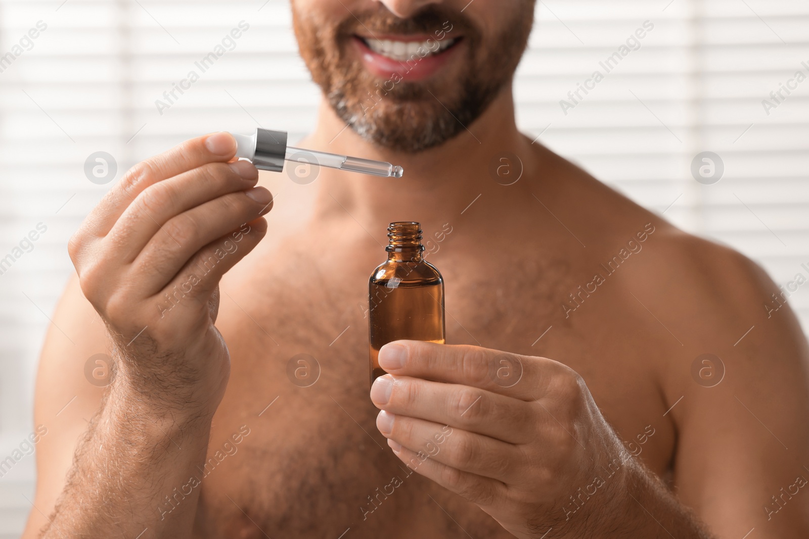 Photo of Smiling man with cosmetic serum indoors, selective focus