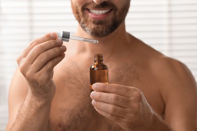 Photo of Smiling man with cosmetic serum indoors, selective focus