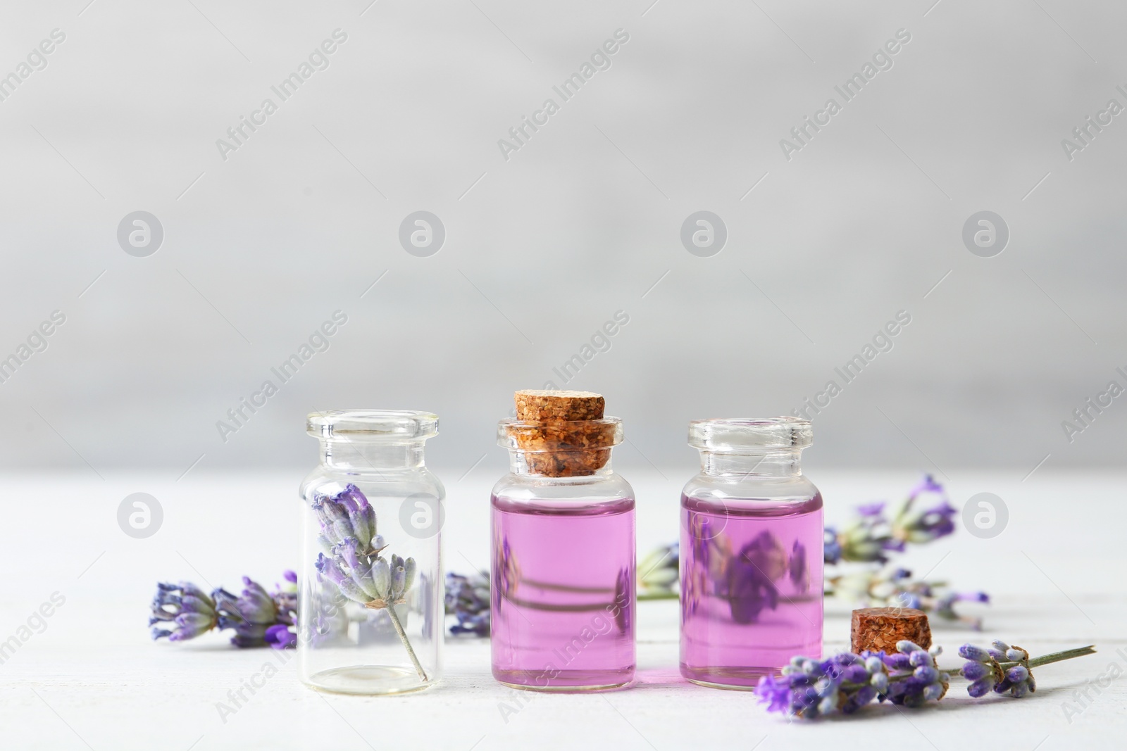 Photo of Bottles with essential oil and lavender flowers on white wooden table