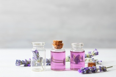 Bottles with essential oil and lavender flowers on white wooden table