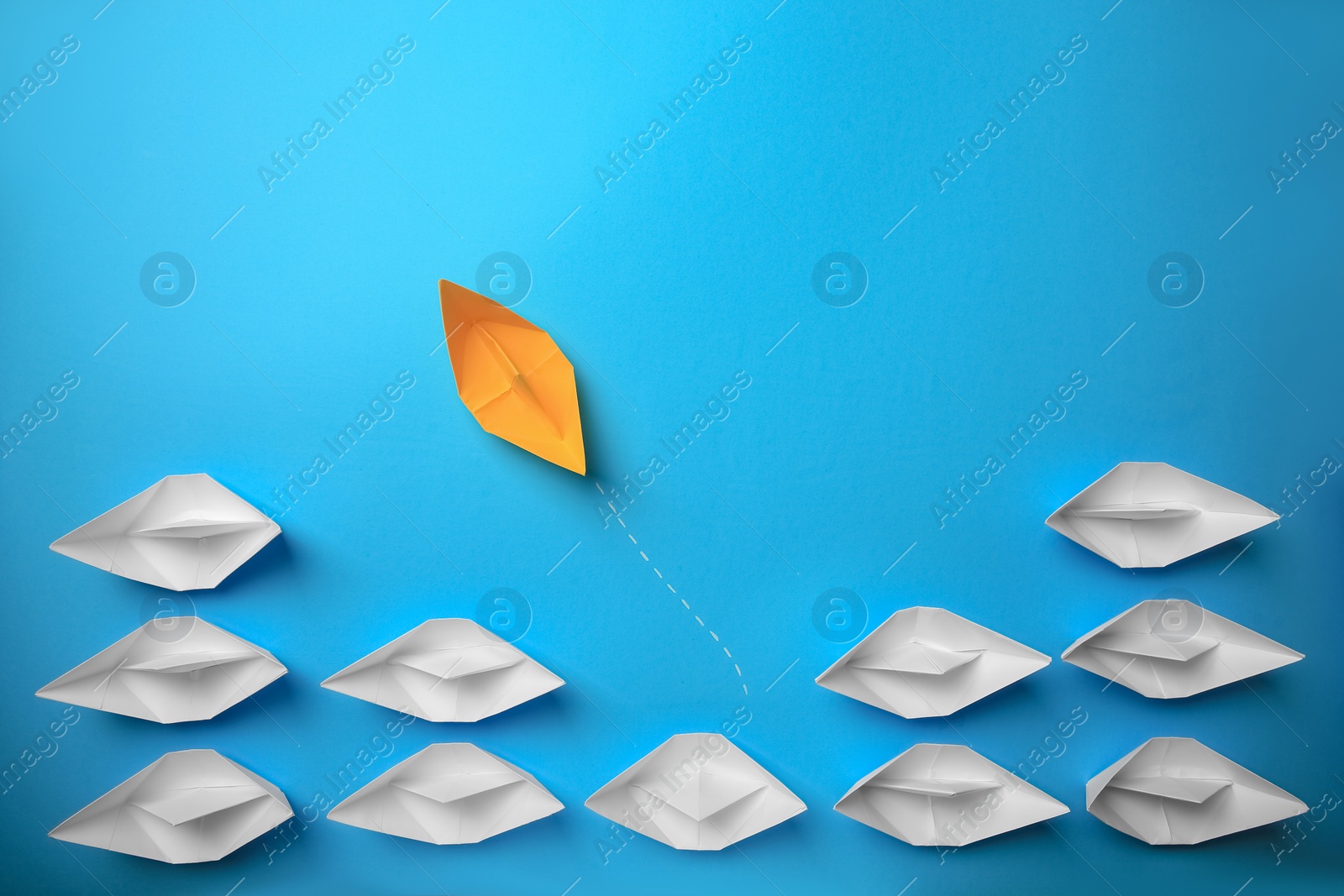 Photo of Yellow paper boat floating away from others on light blue background, flat lay. Uniqueness concept