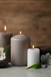 Beautiful composition with burning candles, spa stones and flowers on light grey table