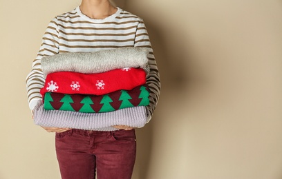 Photo of Woman holding stack of winter clothes on color background. Space for text