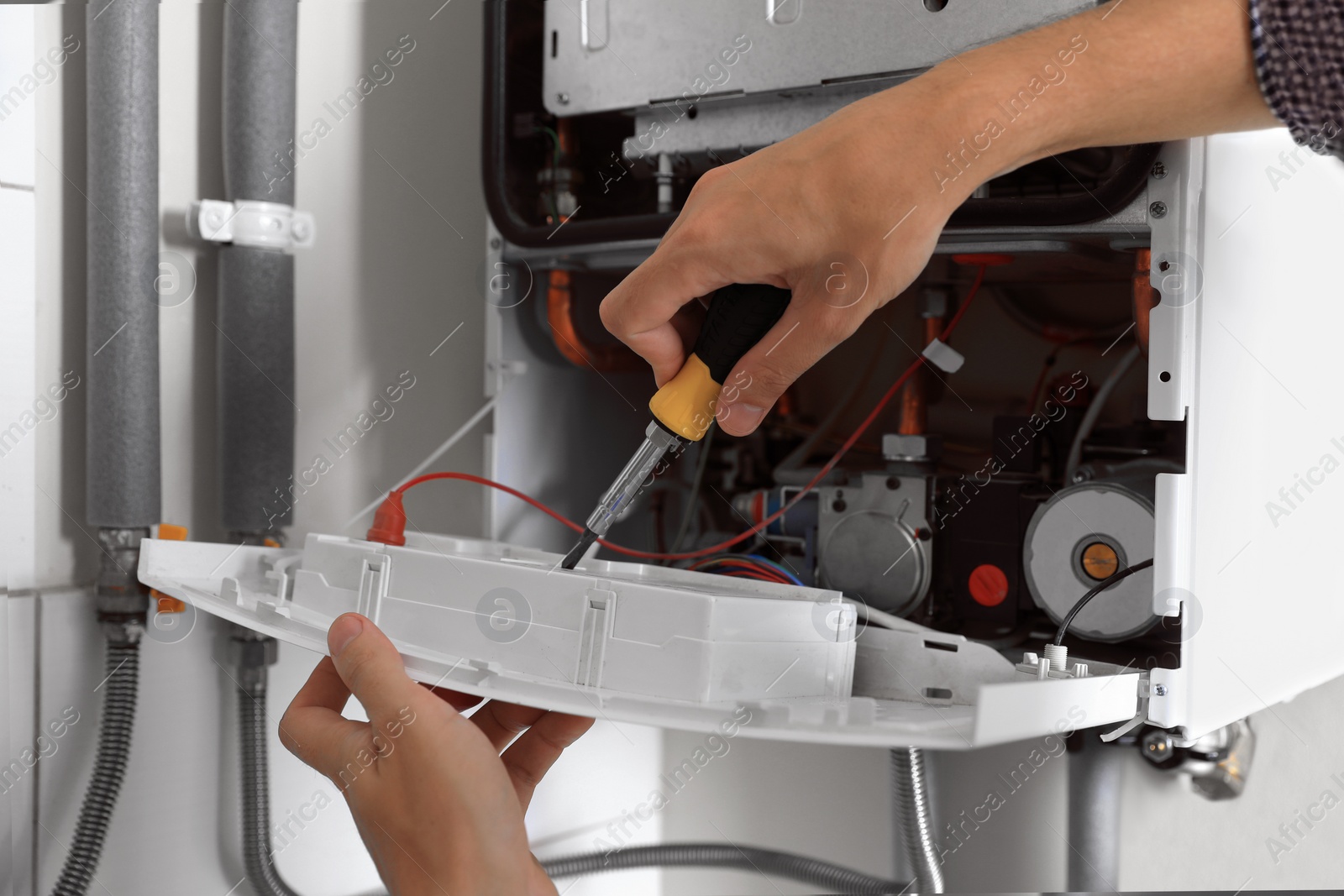 Photo of Man repairing gas boiler with screwdriver indoors, closeup