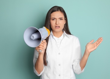 Photo of Young female doctor with megaphone on color background