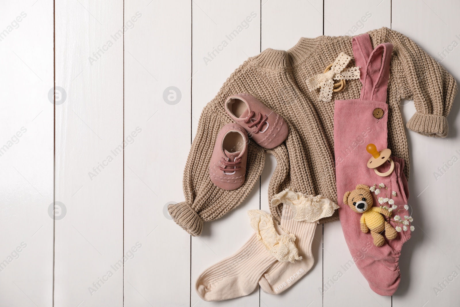 Photo of Flat lay composition with children's clothes, shoes and toy on white wooden table. Space for text