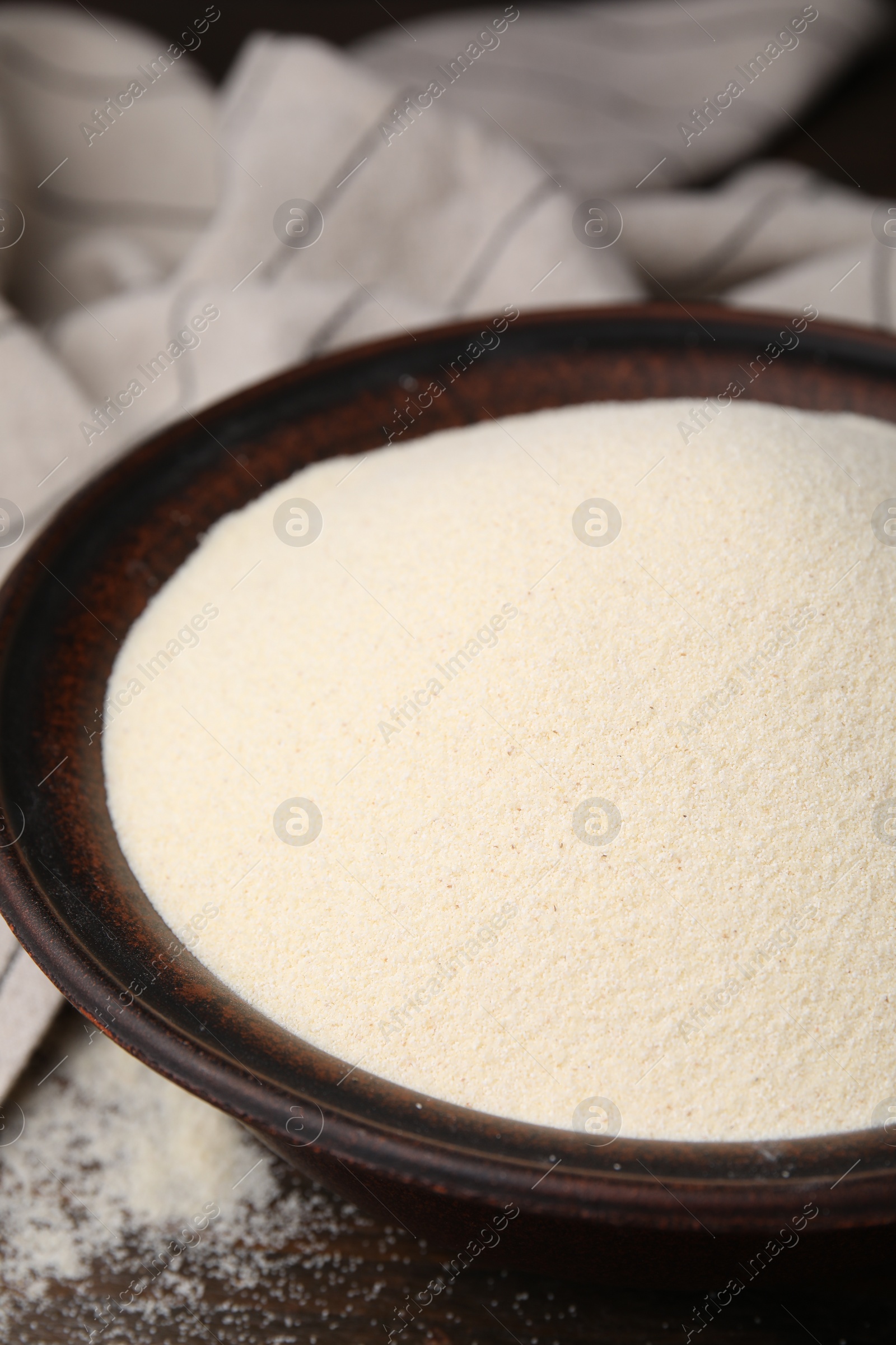 Photo of Uncooked organic semolina in bowl on wooden table, closeup