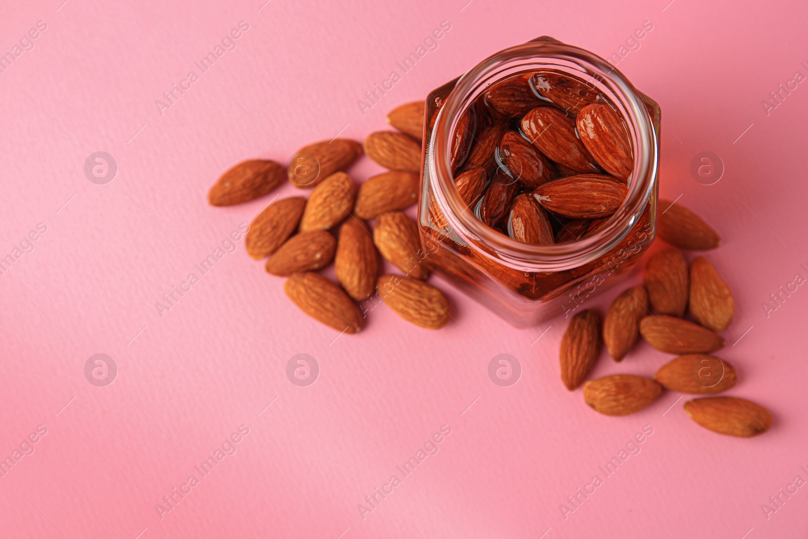 Photo of Jar with almonds and honey on pink background, above view. Space for text
