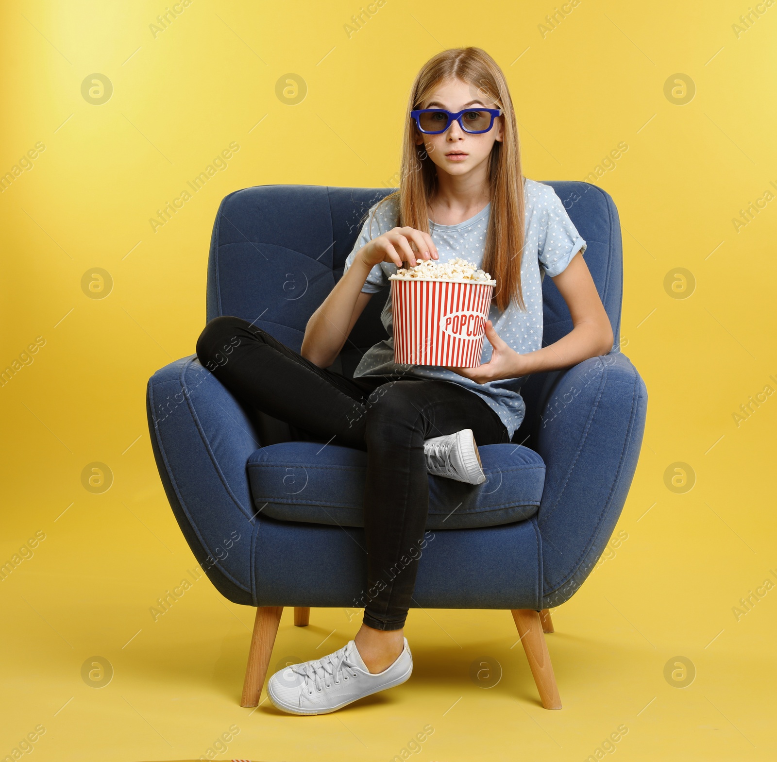 Photo of Emotional teenage girl with 3D glasses and popcorn sitting in armchair during cinema show on color background