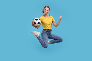 Photo of Happy fan with football ball jumping on light blue background