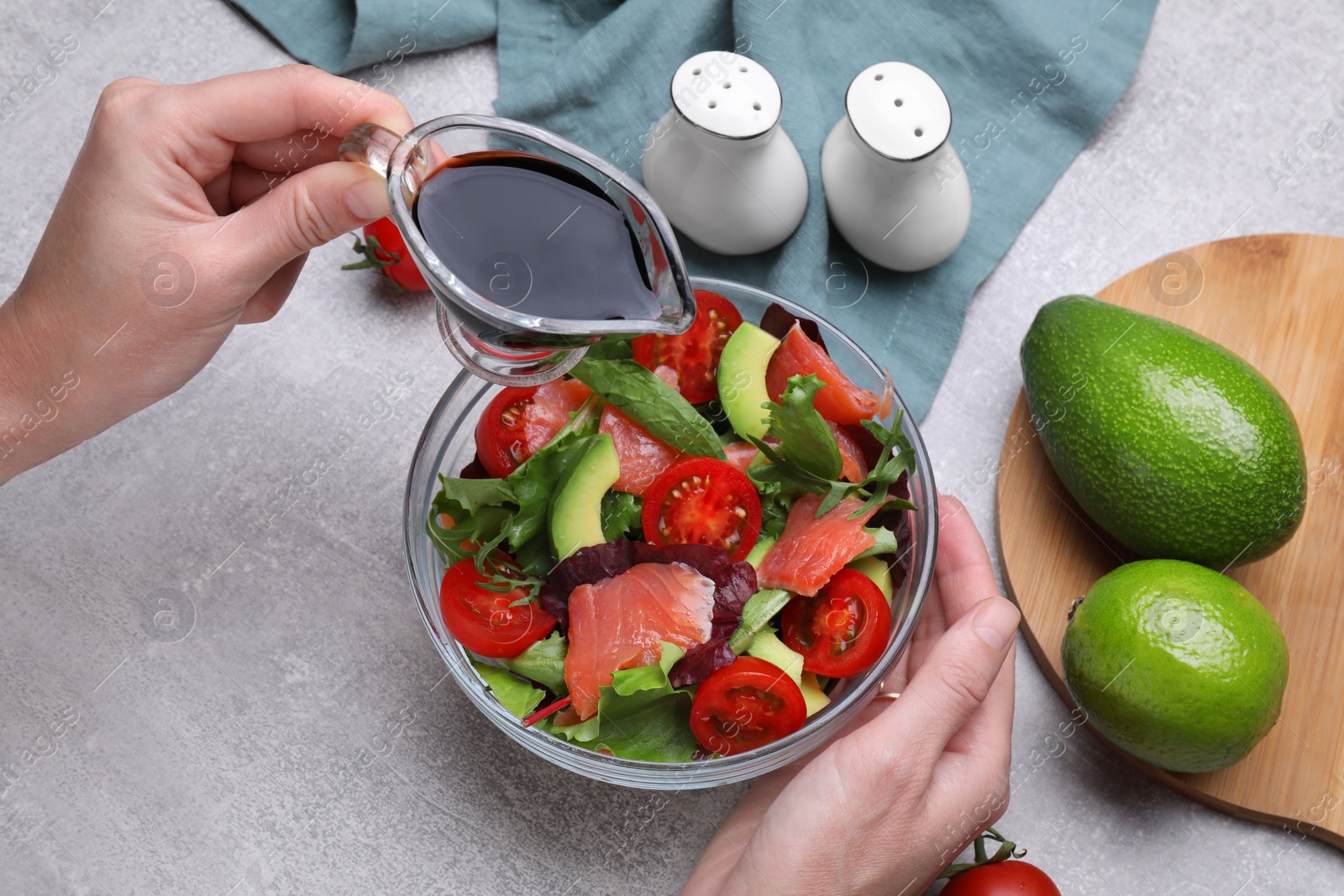 Photo of Woman adding soy sauce to tasty salad at grey table, closeup