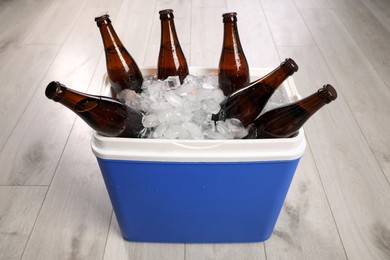 Photo of Blue plastic cool box with ice cubes and beer on wooden floor