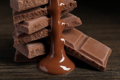 Photo of Pieces of milk chocolate with tasty paste on wooden table, closeup