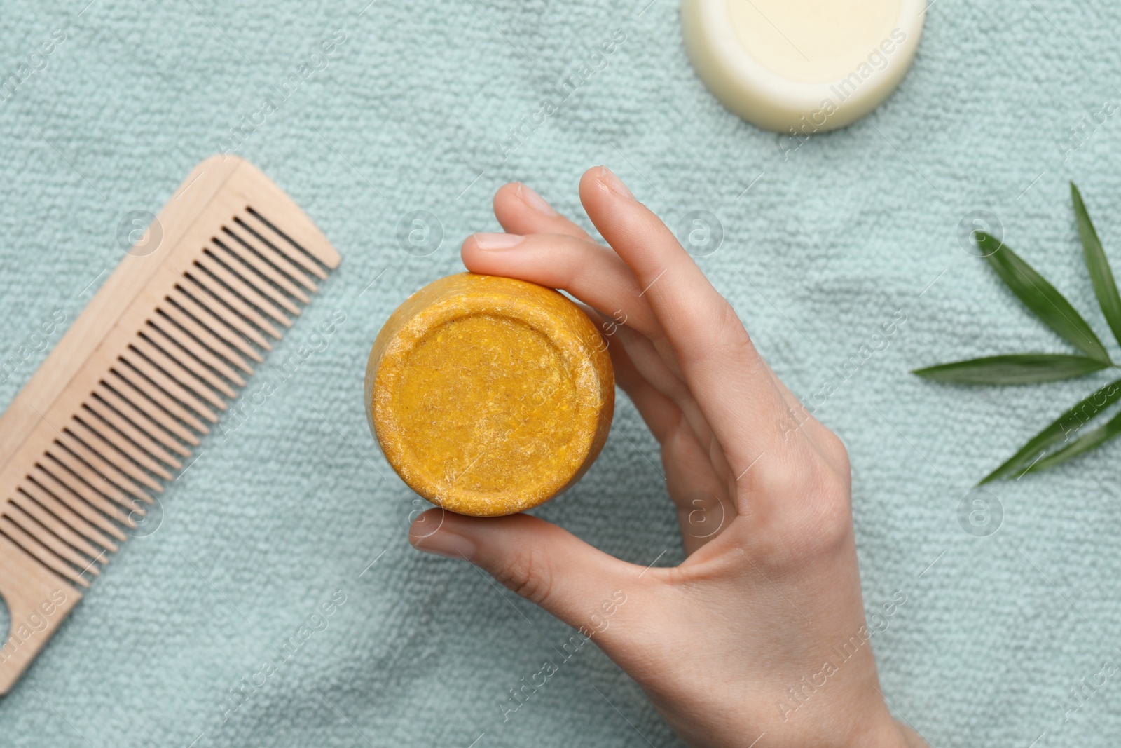 Photo of Woman holding solid shampoo bar near light blue tablecloth, top view. Hair care