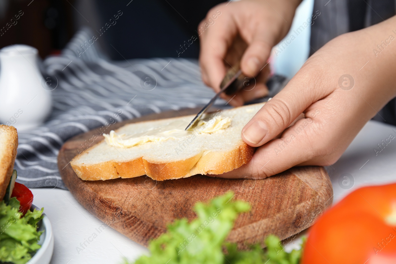 Photo of Woman spreading butter on sandwich at white table, closeup