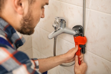 Photo of Professional plumber fixing bath tap indoors, closeup