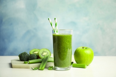 Photo of Delicious green juice and fresh ingredients on white table against light blue background