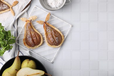 Photo of Delicious pears baked in puff pastry with powdered sugar served on white tiled table, flat lay. Space for text