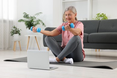 Photo of Senior woman exercising with dumbbells while watching online tutorial at home. Sports equipment