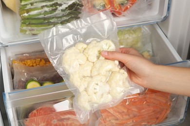 Woman putting vacuum bag with cauliflowers into fridge, closeup. Food storage