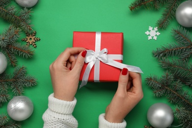 Woman with gift box near fir tree branches and Christmas decor on green background, top view