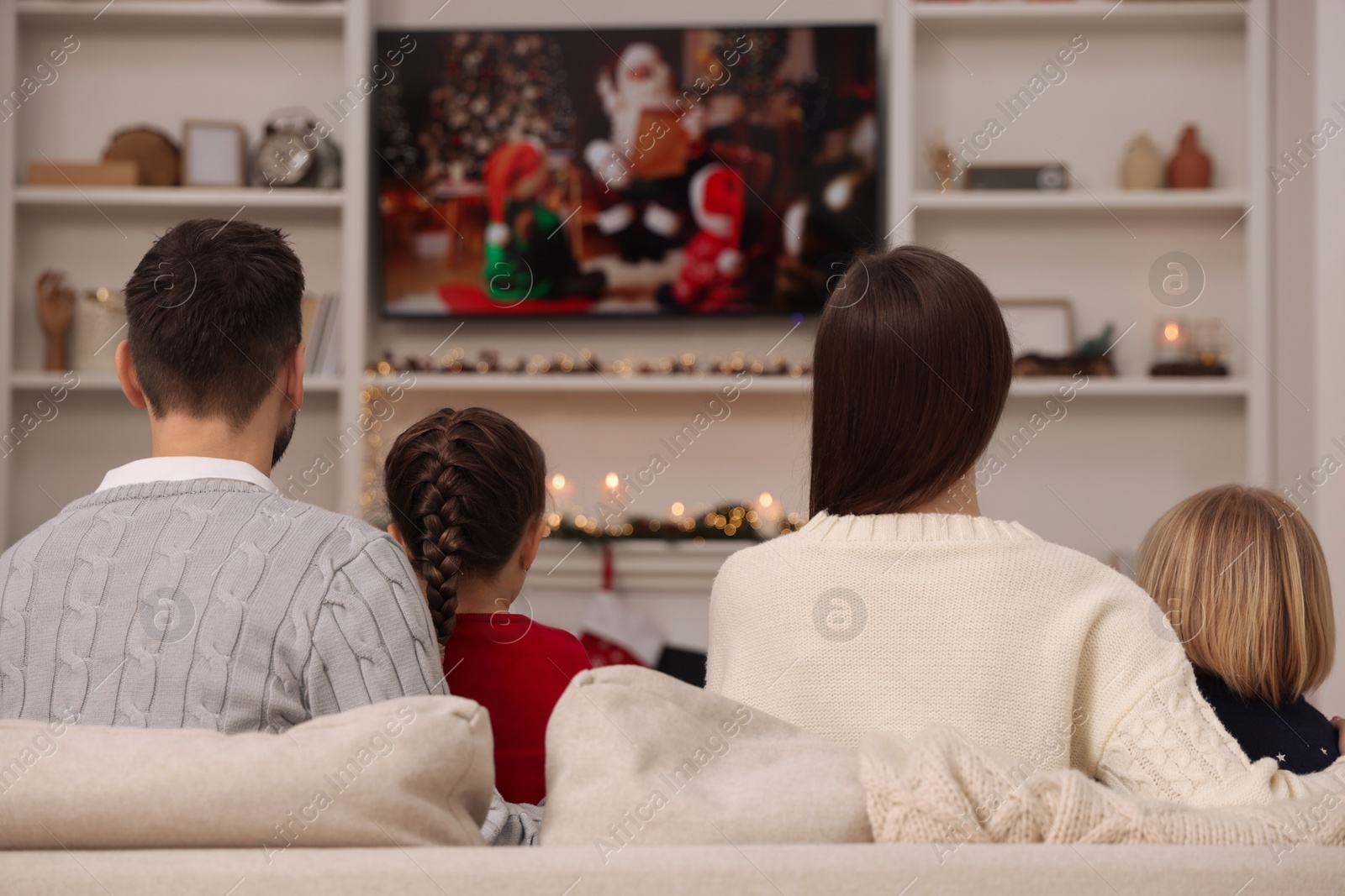 Photo of Family watching Christmas movie via TV in cosy room, back view. Winter holidays atmosphere