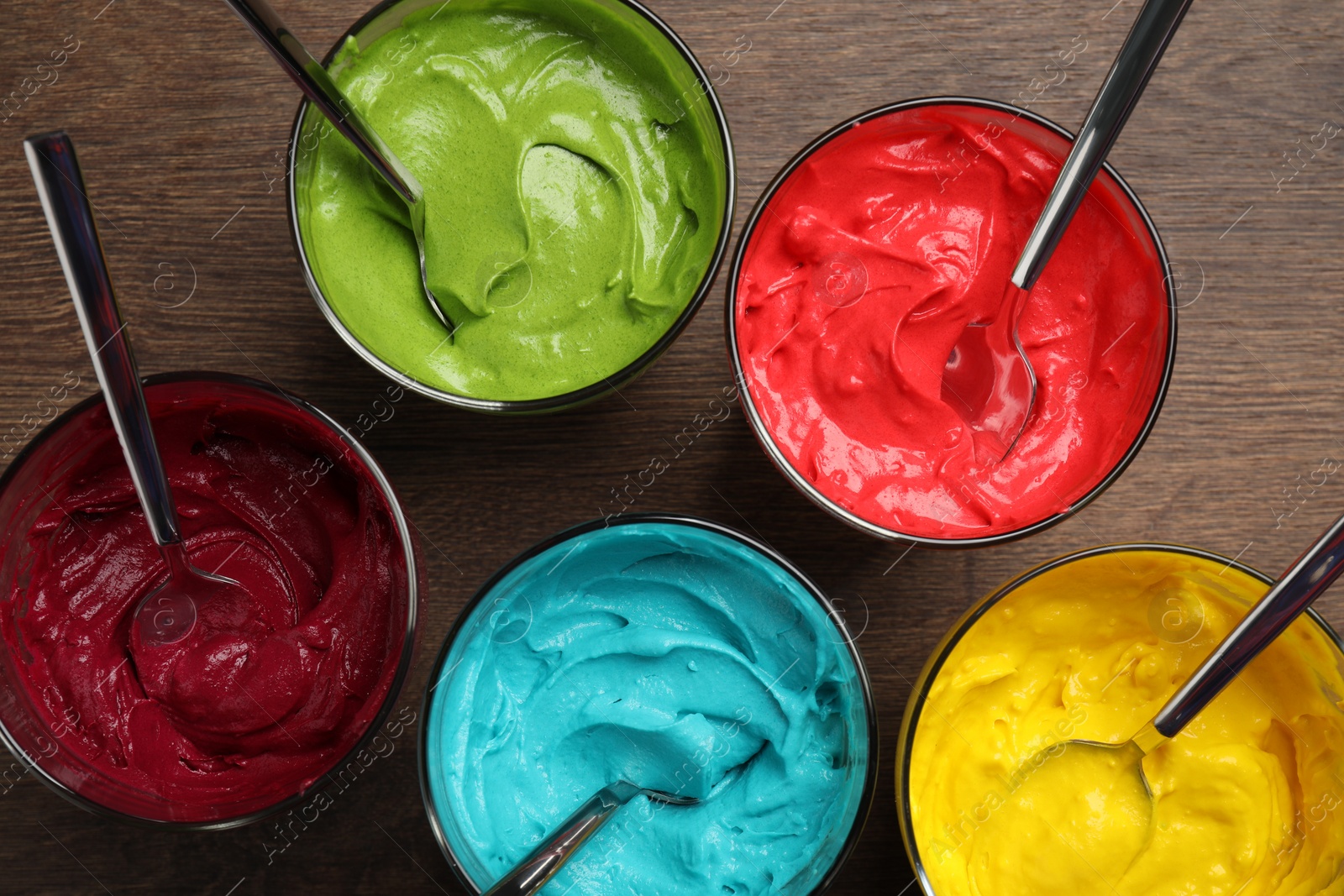 Photo of Glasses of different cream with food coloring on wooden table, flat lay