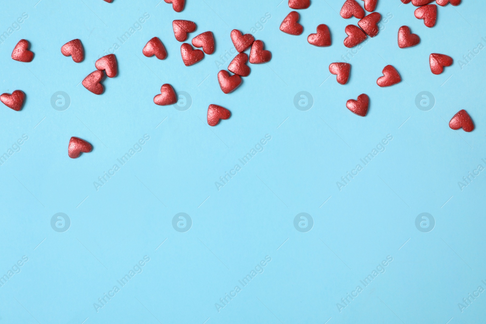 Photo of Bright heart shaped sprinkles on light blue background, flat lay. Space for text