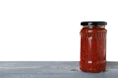 Photo of Jar of vegetable sauce on blue wooden table against white background. Pickled food