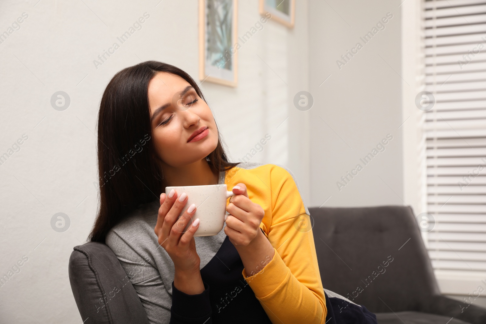 Photo of Young woman with cup of drink relaxing at home