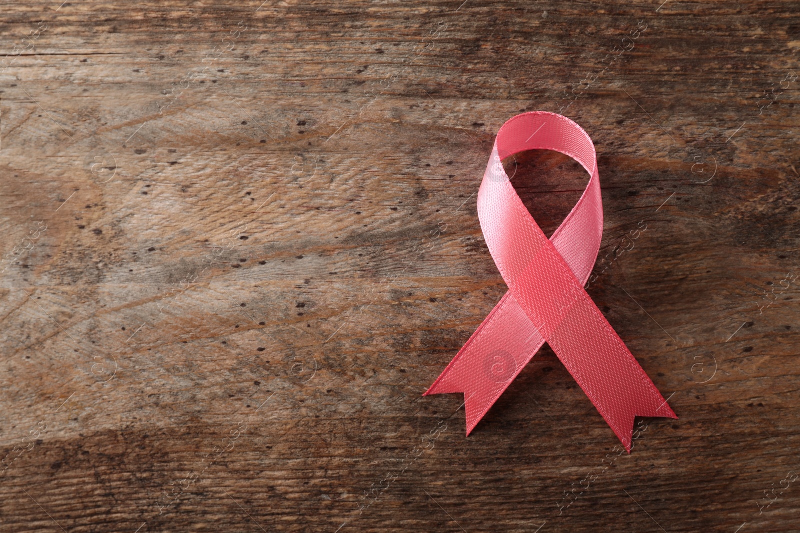 Photo of Pink ribbon on wooden background, top view with space for text. Breast cancer awareness concept