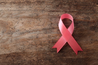 Pink ribbon on wooden background, top view with space for text. Breast cancer awareness concept