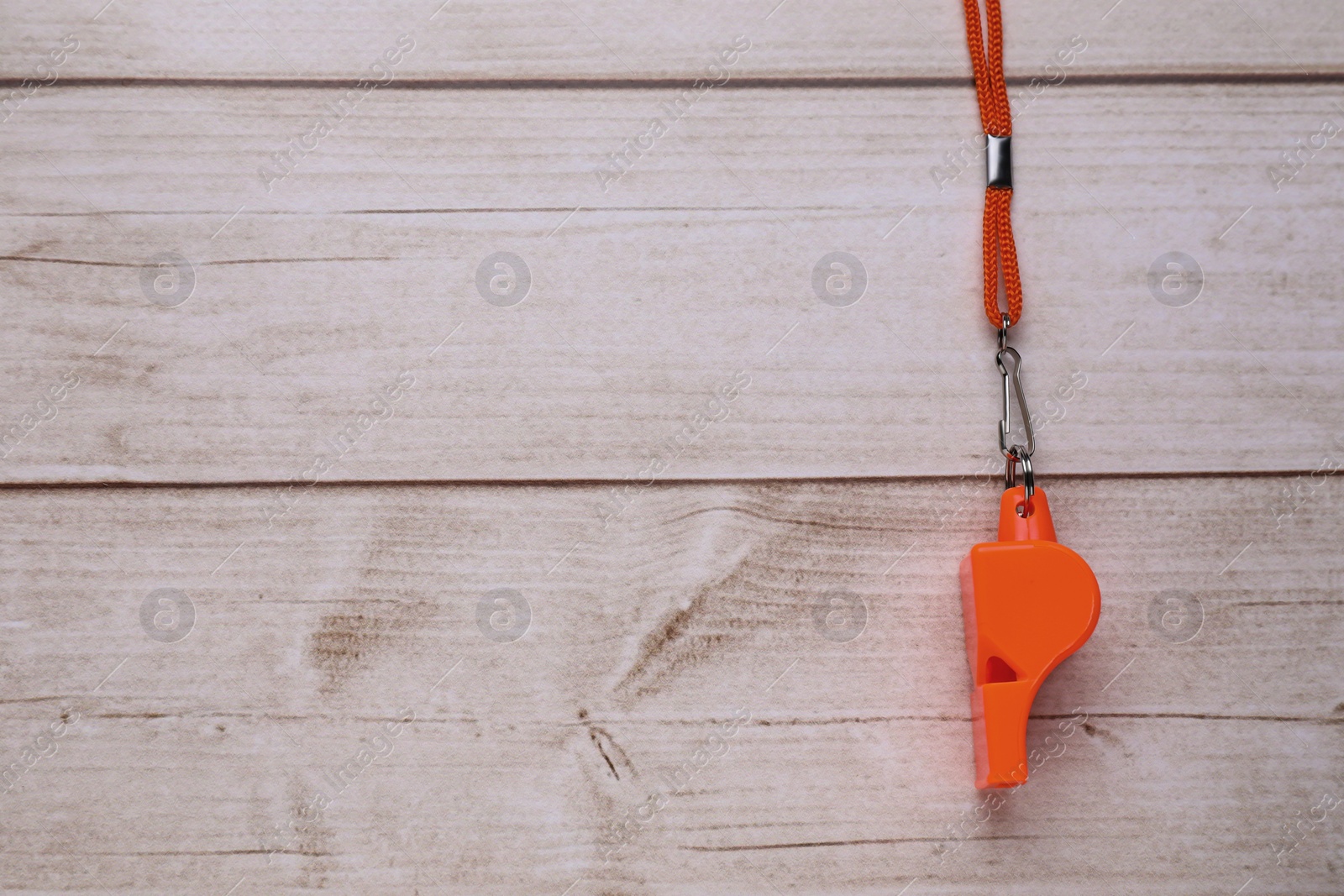 Photo of One orange whistle with cord on light wooden table, top view. Space for text