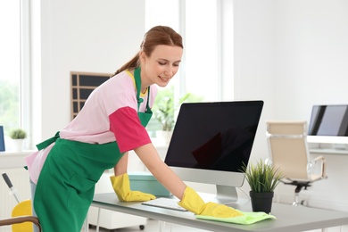 Photo of Young woman in apron and gloves cleaning office