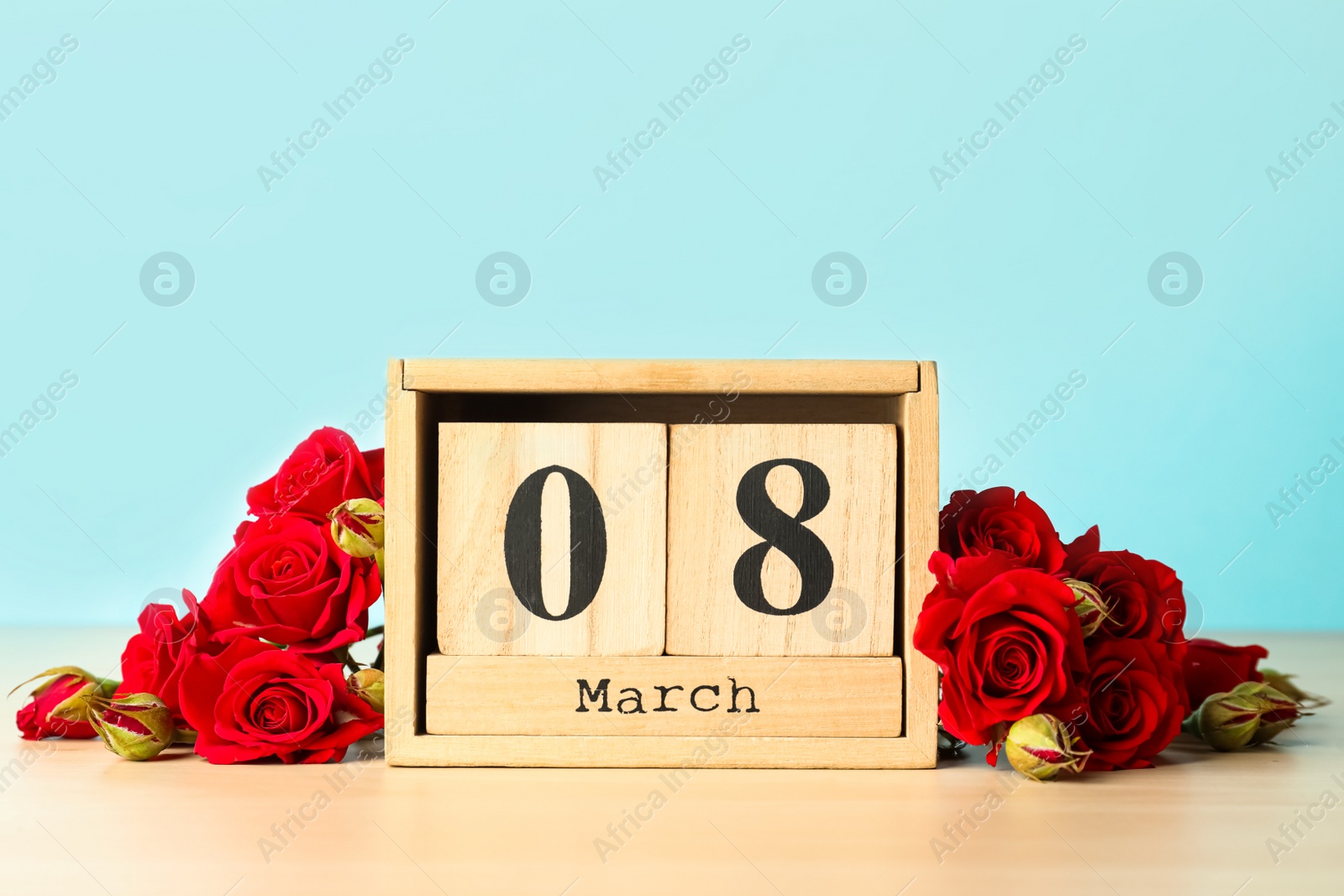 Photo of Wooden block calendar with date 8th of March and roses on table against light blue background, space for text. International Women's Day