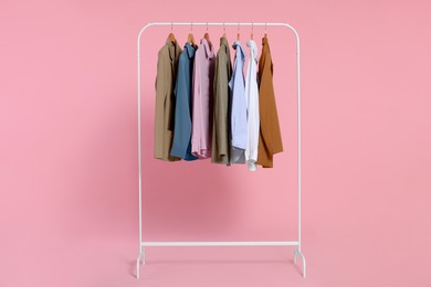 Photo of Rack with stylish clothes on wooden hangers against pink background