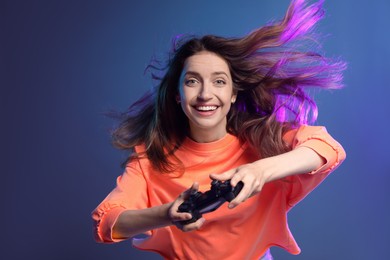 Emotional woman playing video game with controller on dark blue background