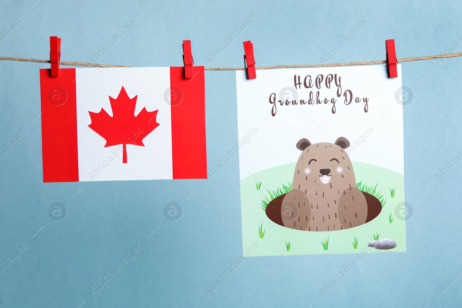 Photo of Happy Groundhog Day greeting card and Canada flag hanging on light blue background