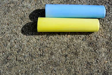 Photo of Yellow and light blue chalk sticks on asphalt, flat lay. Space for text