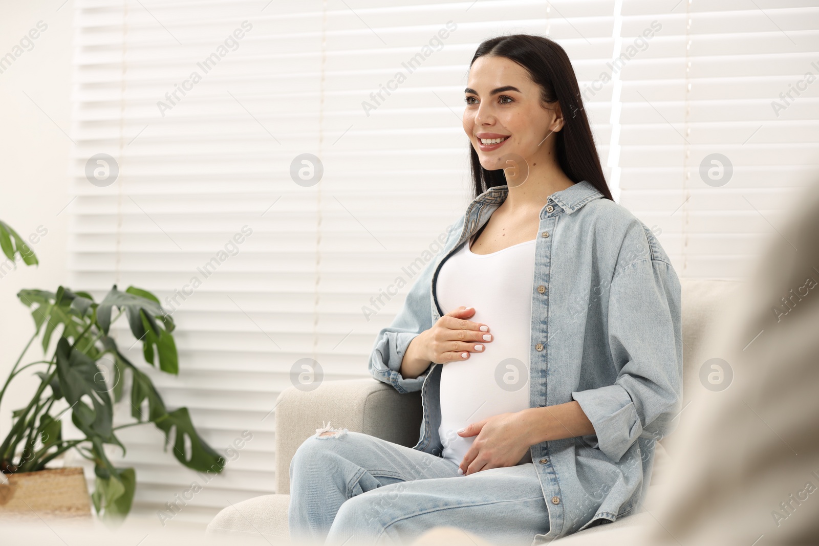 Photo of Happy pregnant woman on sofa at home, space for text