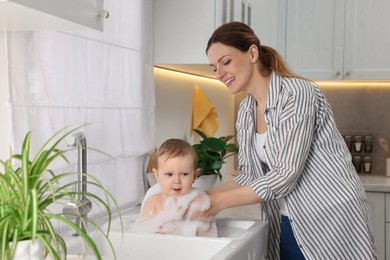 Photo of Mother washing her little baby in sink at home