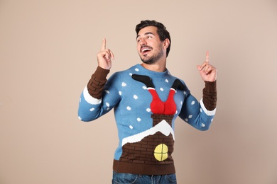 Happy young man in Christmas sweater on beige background