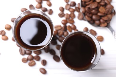 Photo of Glasses of coffee liqueur and beans on white table, flat lay