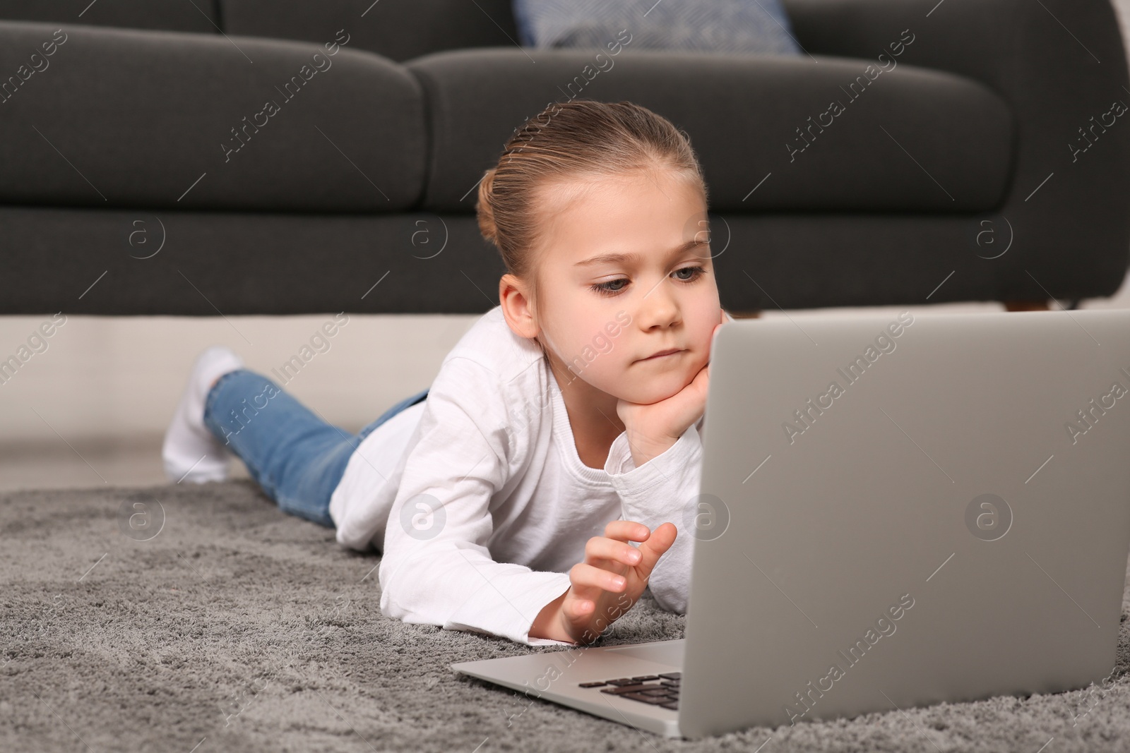 Photo of Little girl using laptop on floor at home. Internet addiction