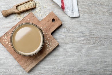 Photo of Tasty sesame paste, seeds and scoop on white wooden table, flat lay. Space for text